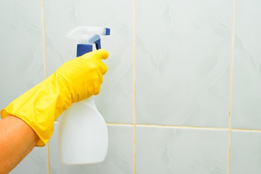 A gloved hand spraying a shower wall with a spray bottle