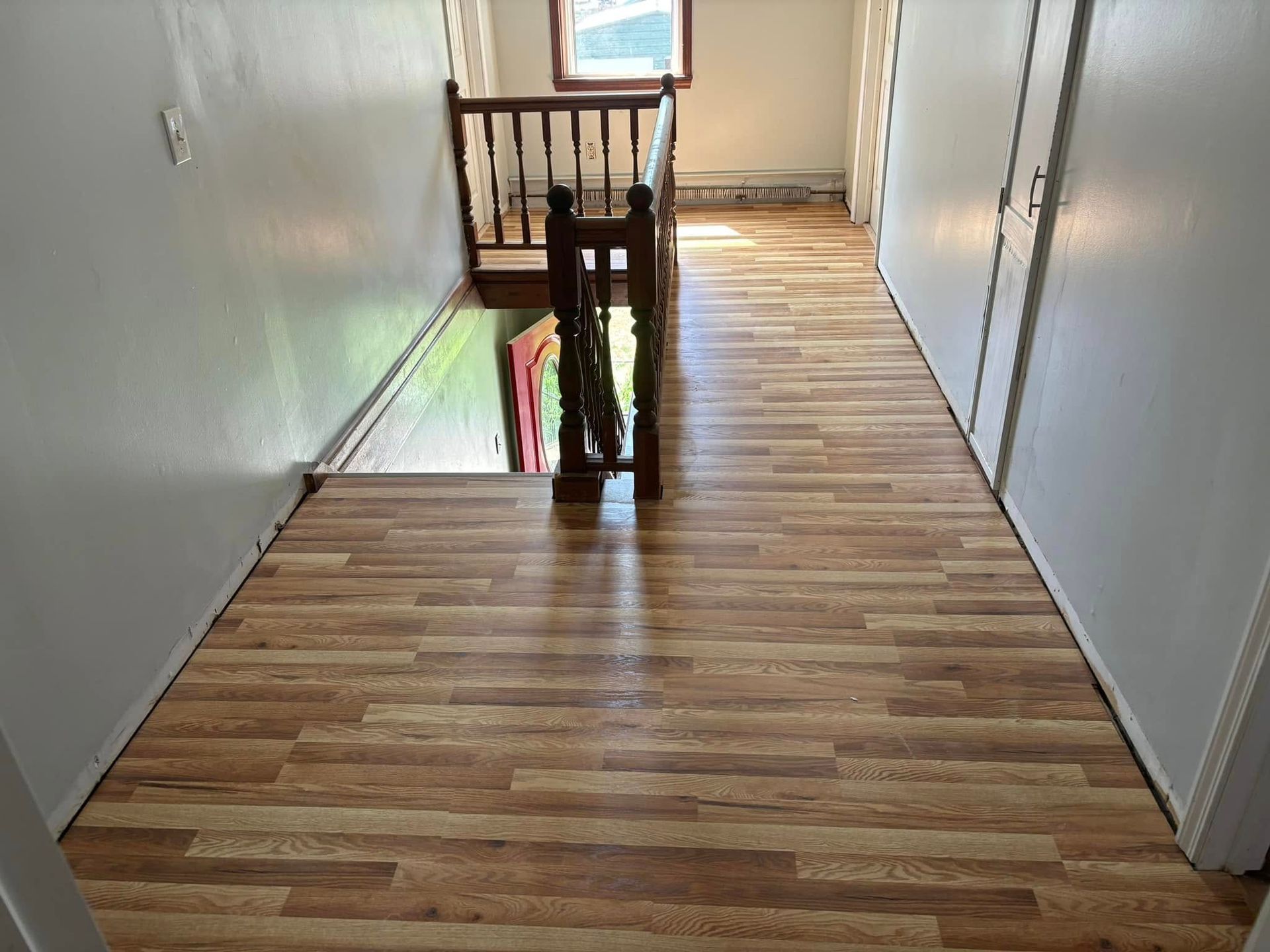 A hallway with a wooden floor and stairs leading up to the second floor.