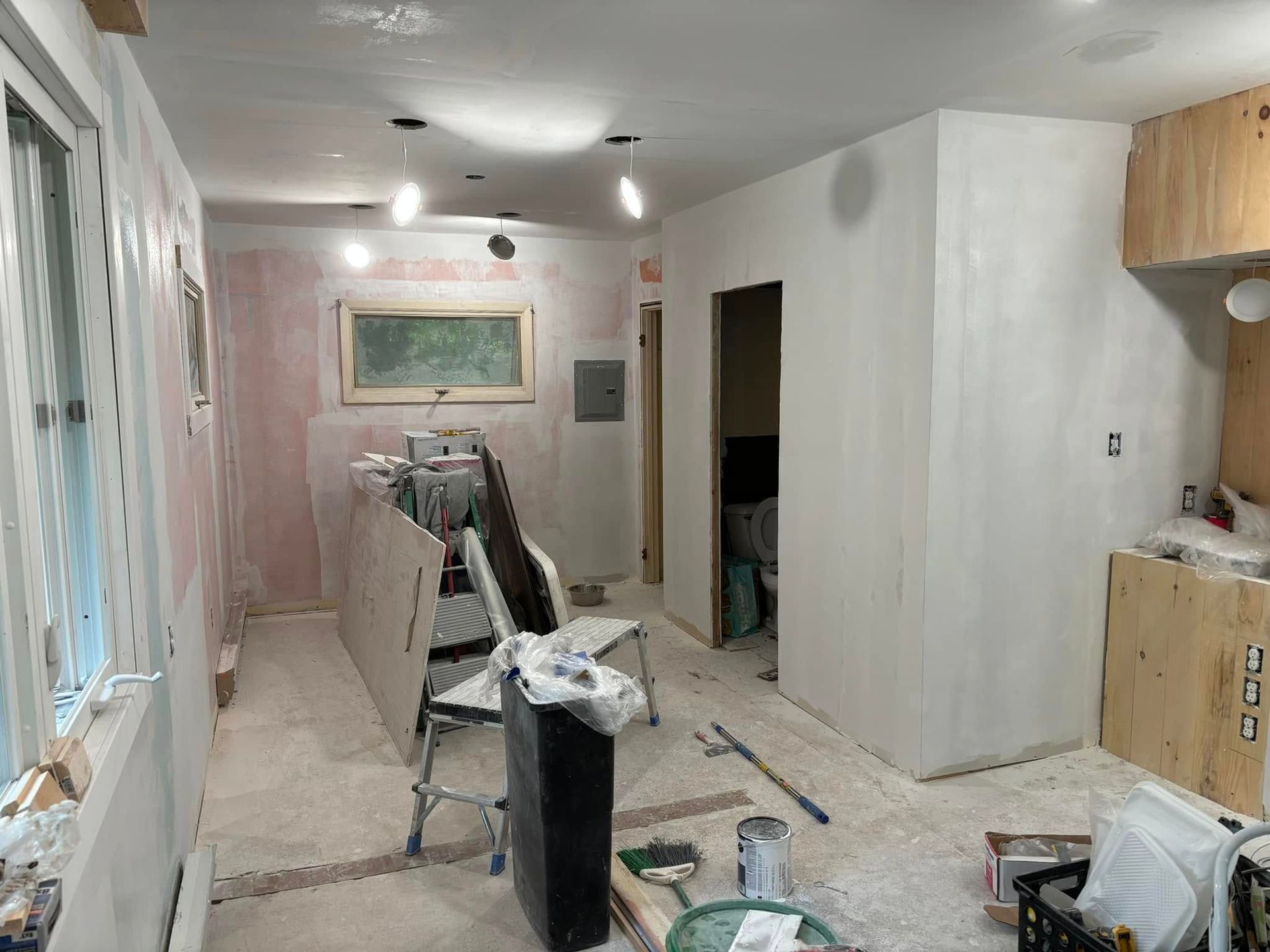 A room with a ladder and a bucket of paint on a bench.