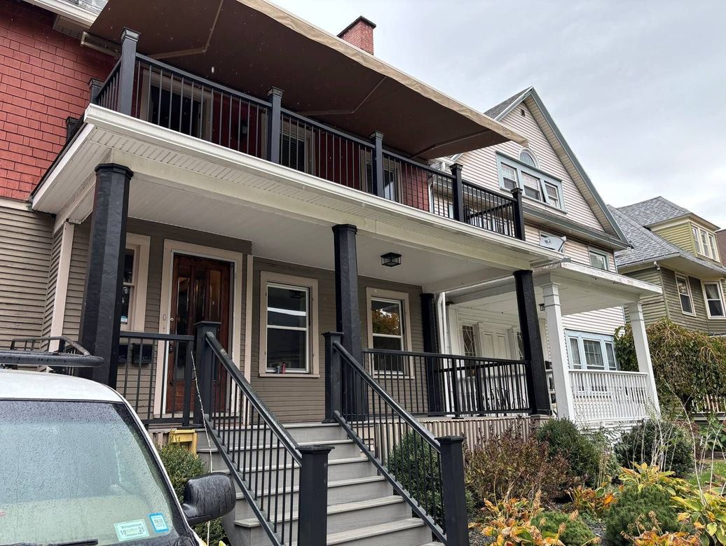 A car is parked in front of a house with a porch and stairs.