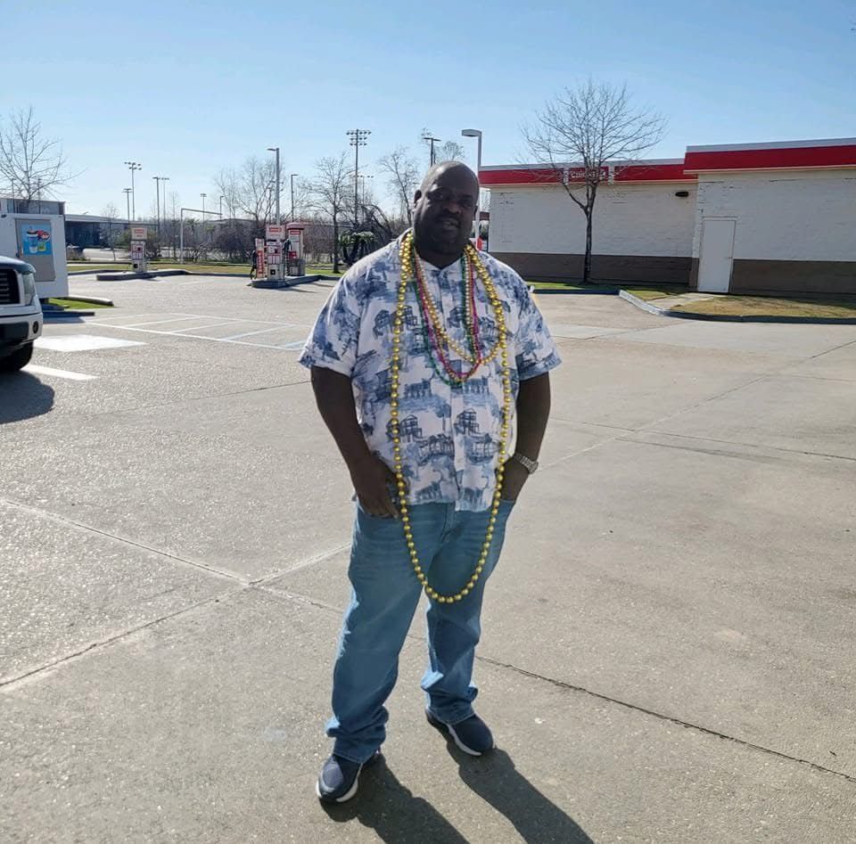 A man wearing a floral shirt and jeans is standing in a parking lot