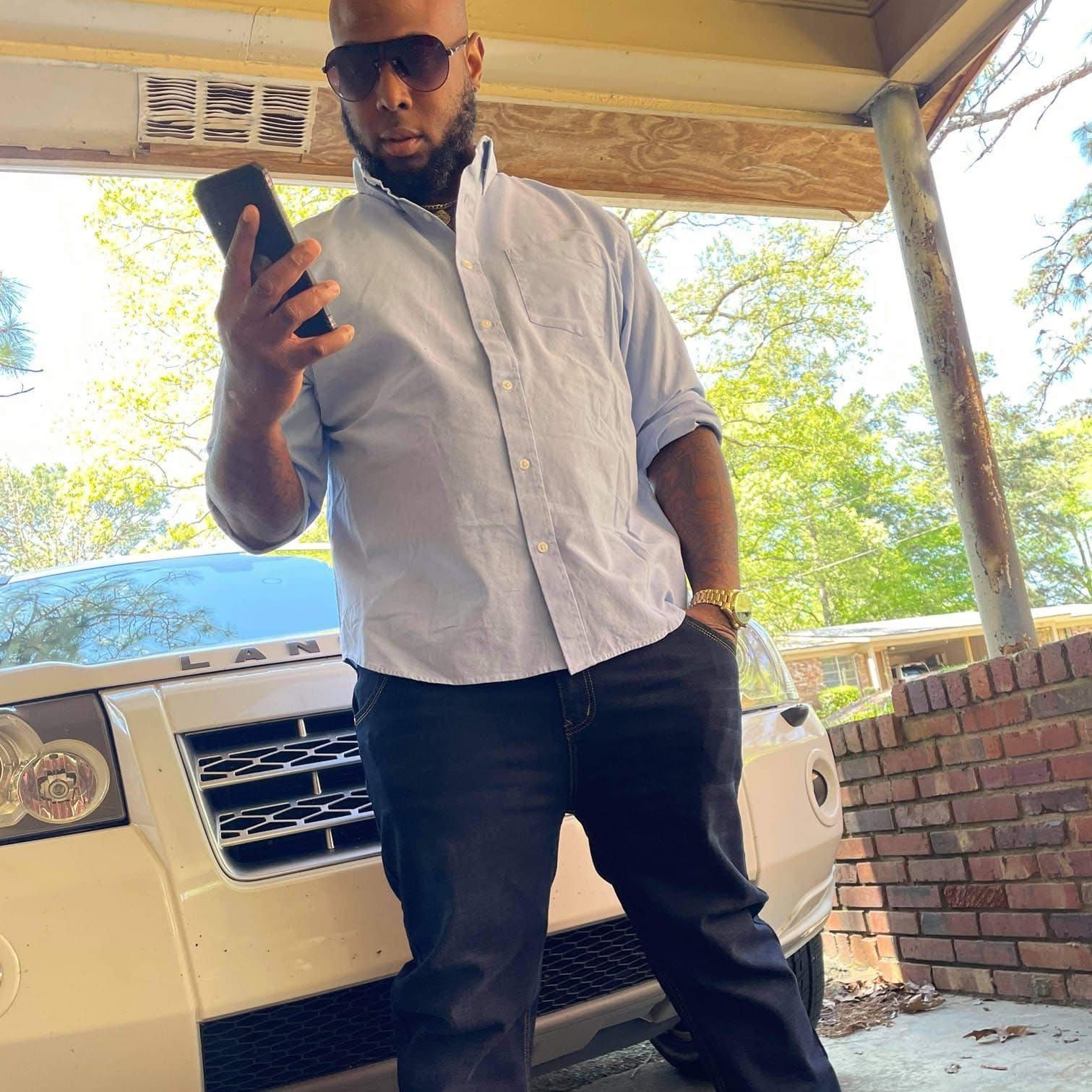 A man is standing in front of a car holding a cell phone.