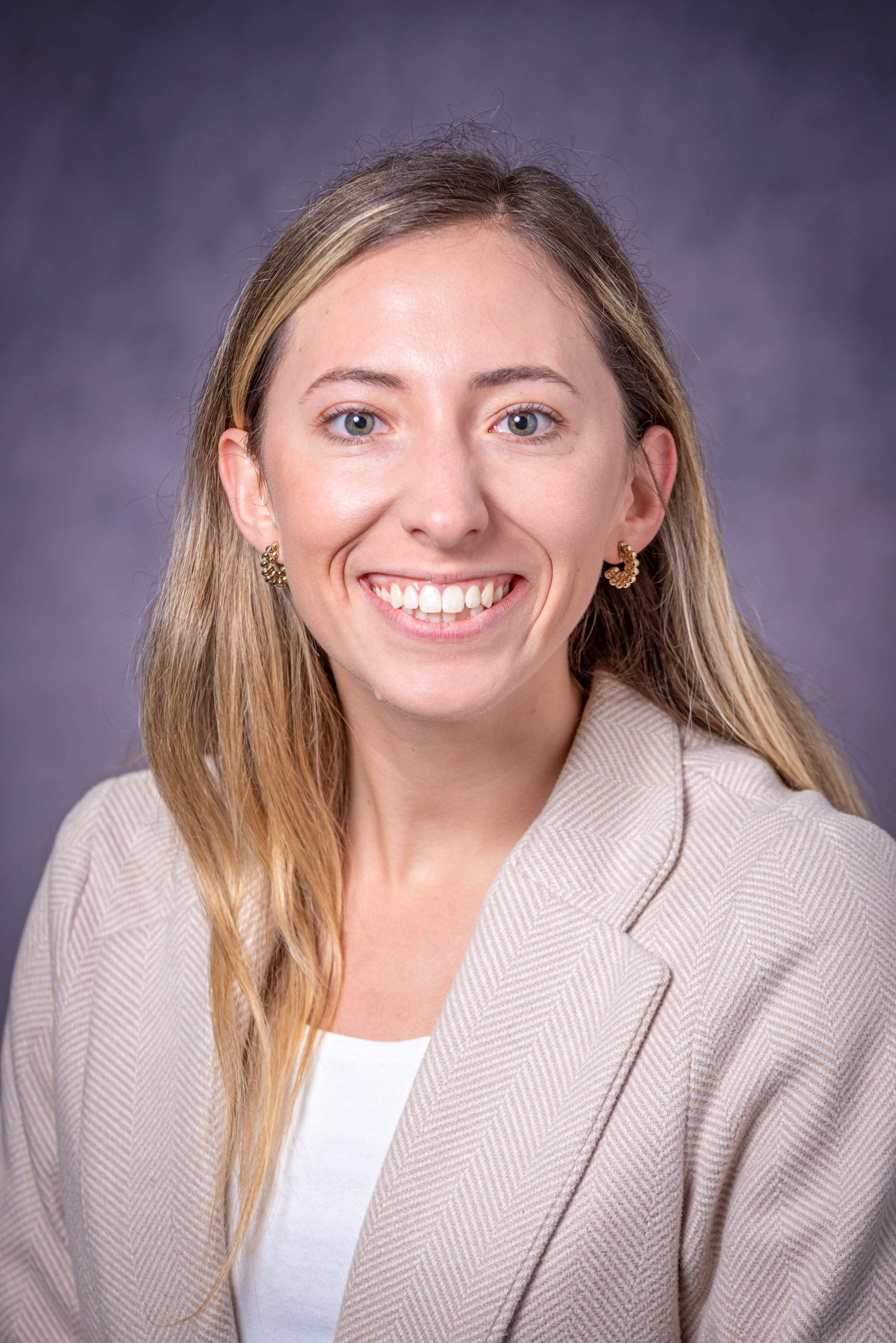 A woman in a tan jacket and white shirt is smiling for the camera.