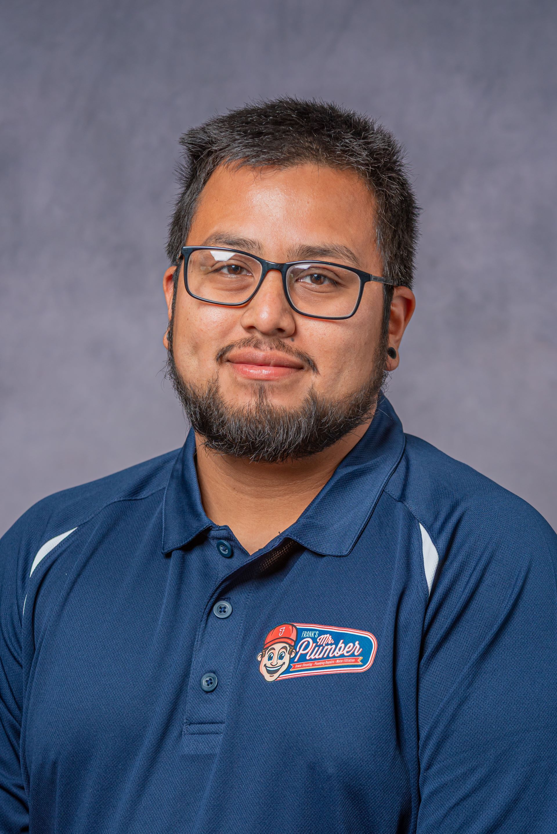 A man with glasses and a beard is wearing a blue polo shirt.