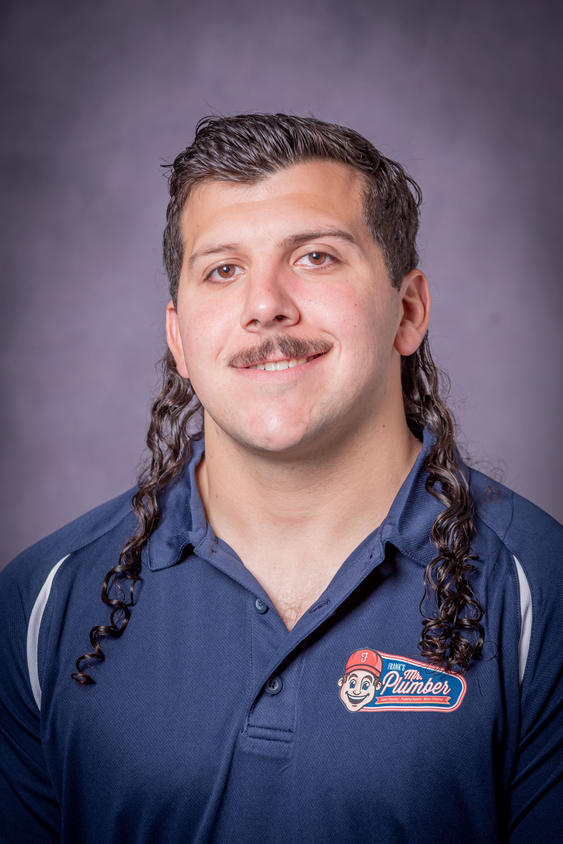 A man with a mullet and a mustache is wearing a blue shirt.