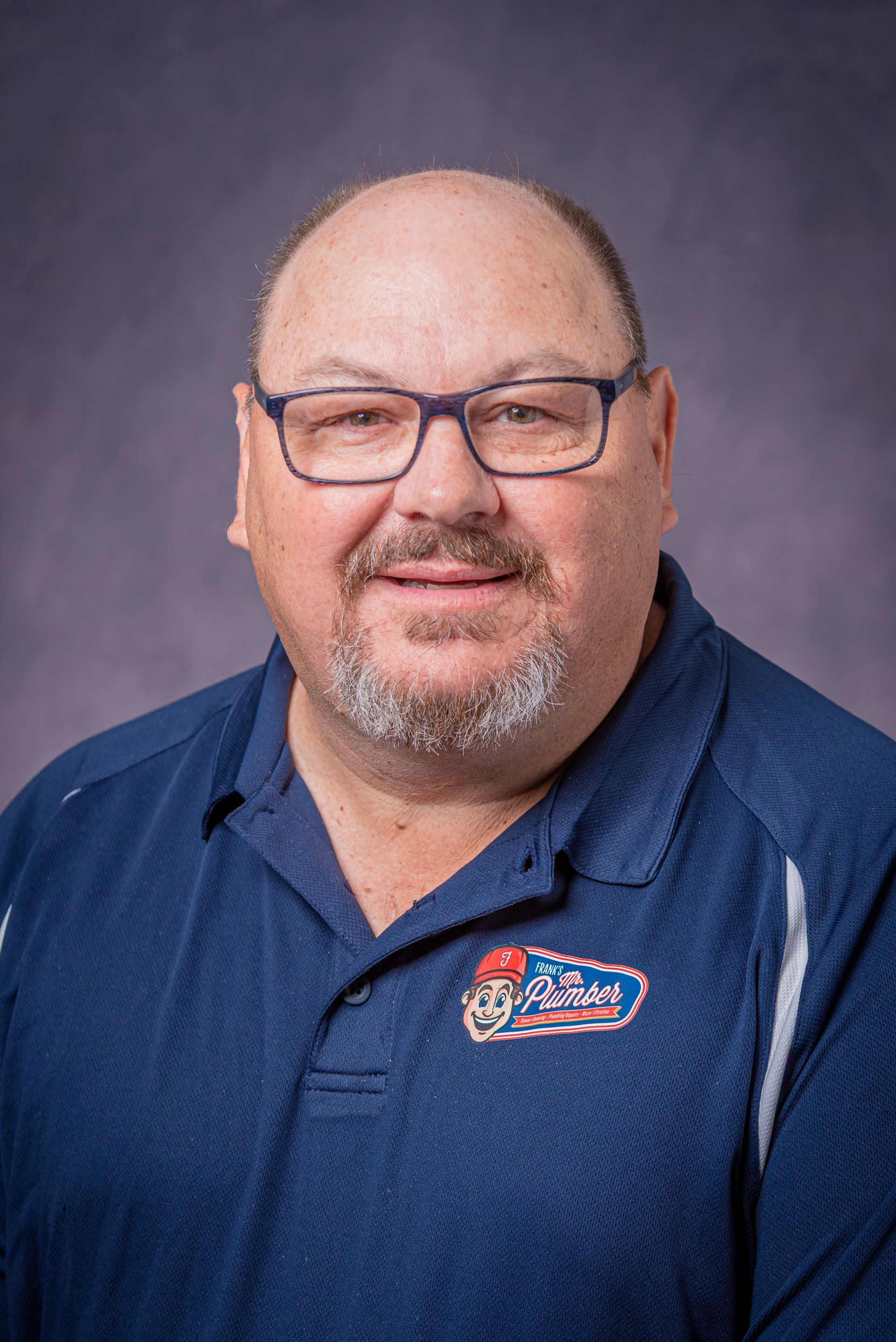 A man wearing glasses and a blue shirt is smiling for the camera.