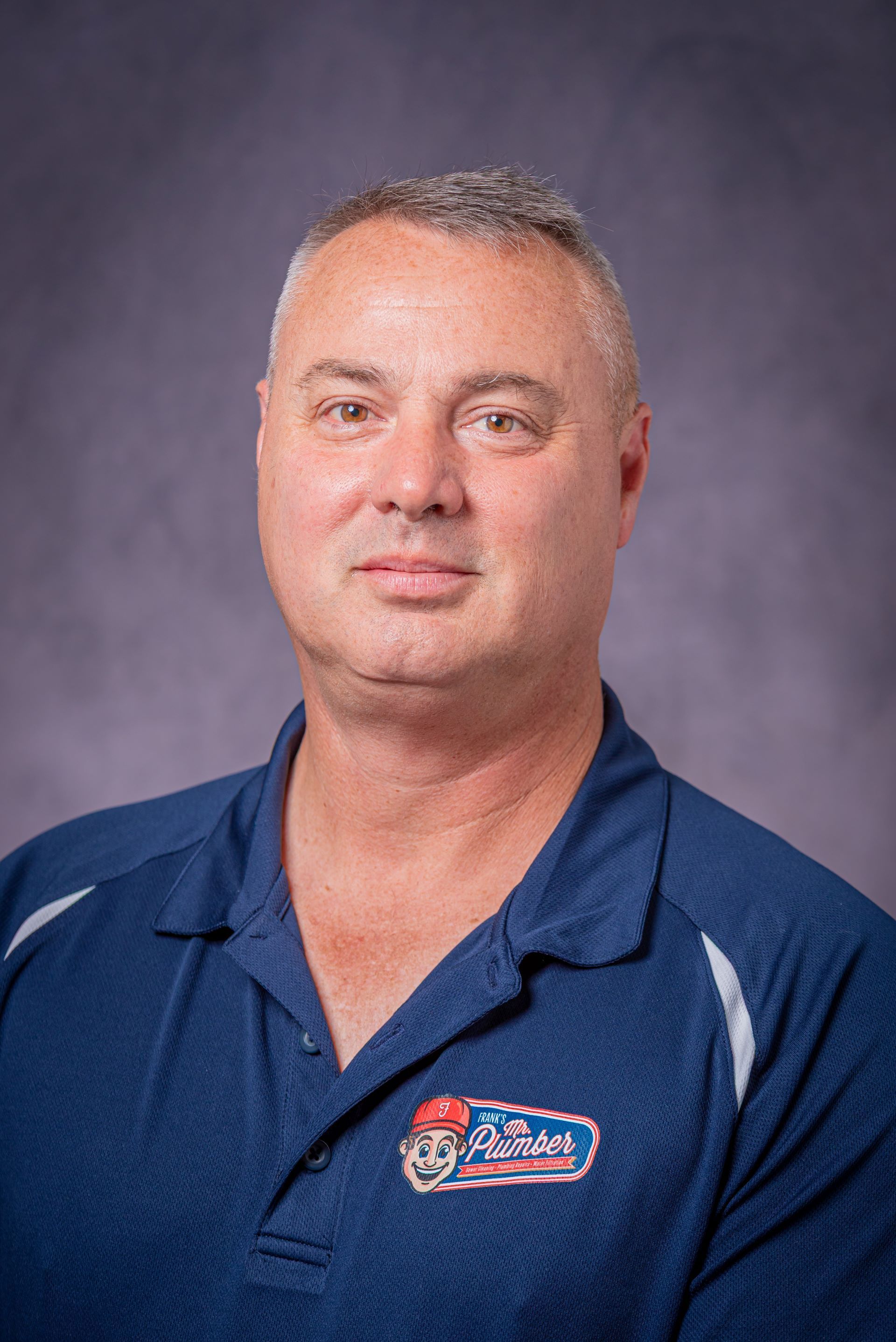 A man in a blue shirt is standing in front of a blue background.