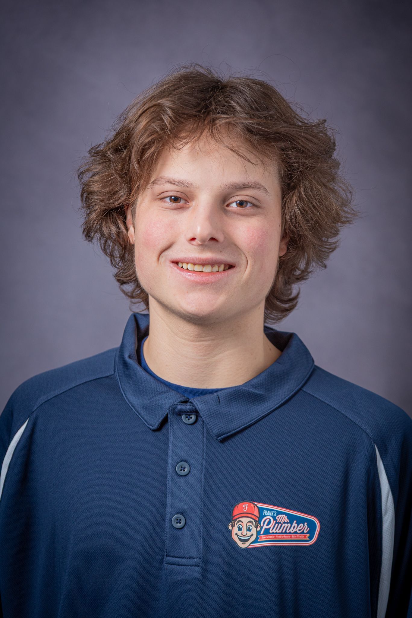 Young person with curly brown hair, smiling, wearing a navy polo shirt with a logo.