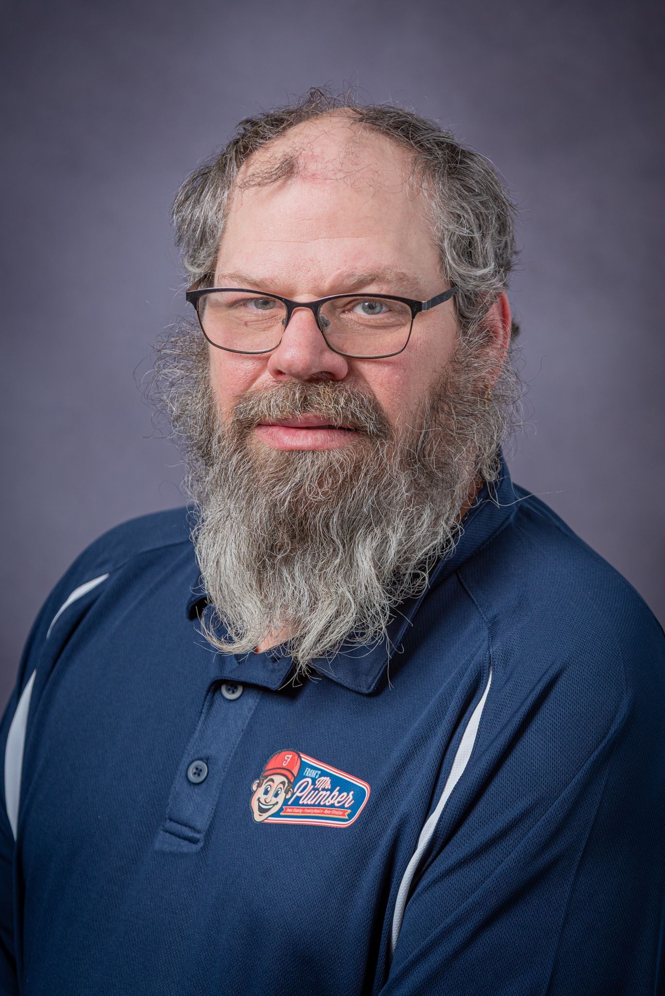 Man with glasses and grey beard in a blue polo shirt.