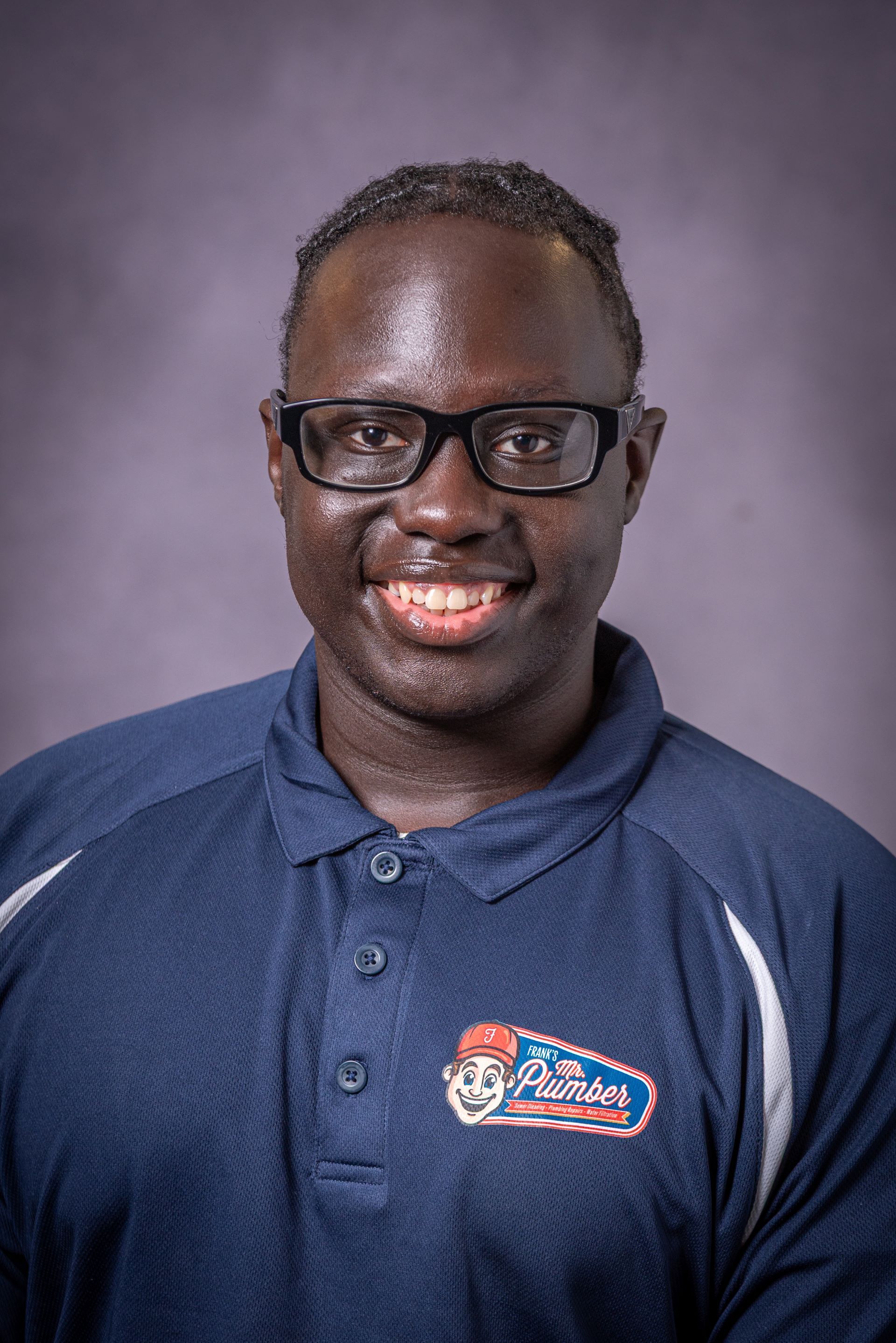 A man wearing glasses and a blue polo shirt is smiling for the camera.