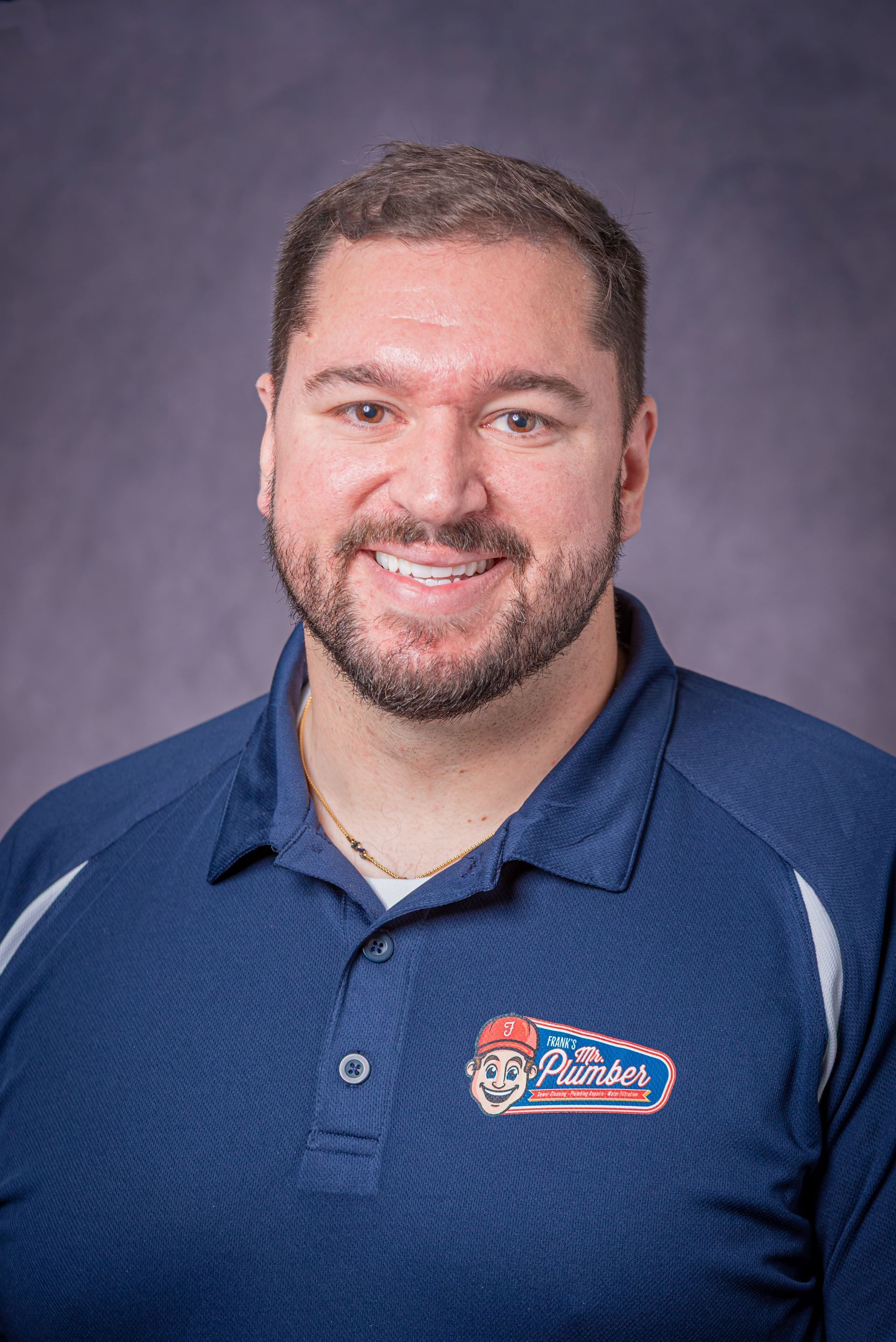 A man with a beard is wearing a blue polo shirt and smiling.