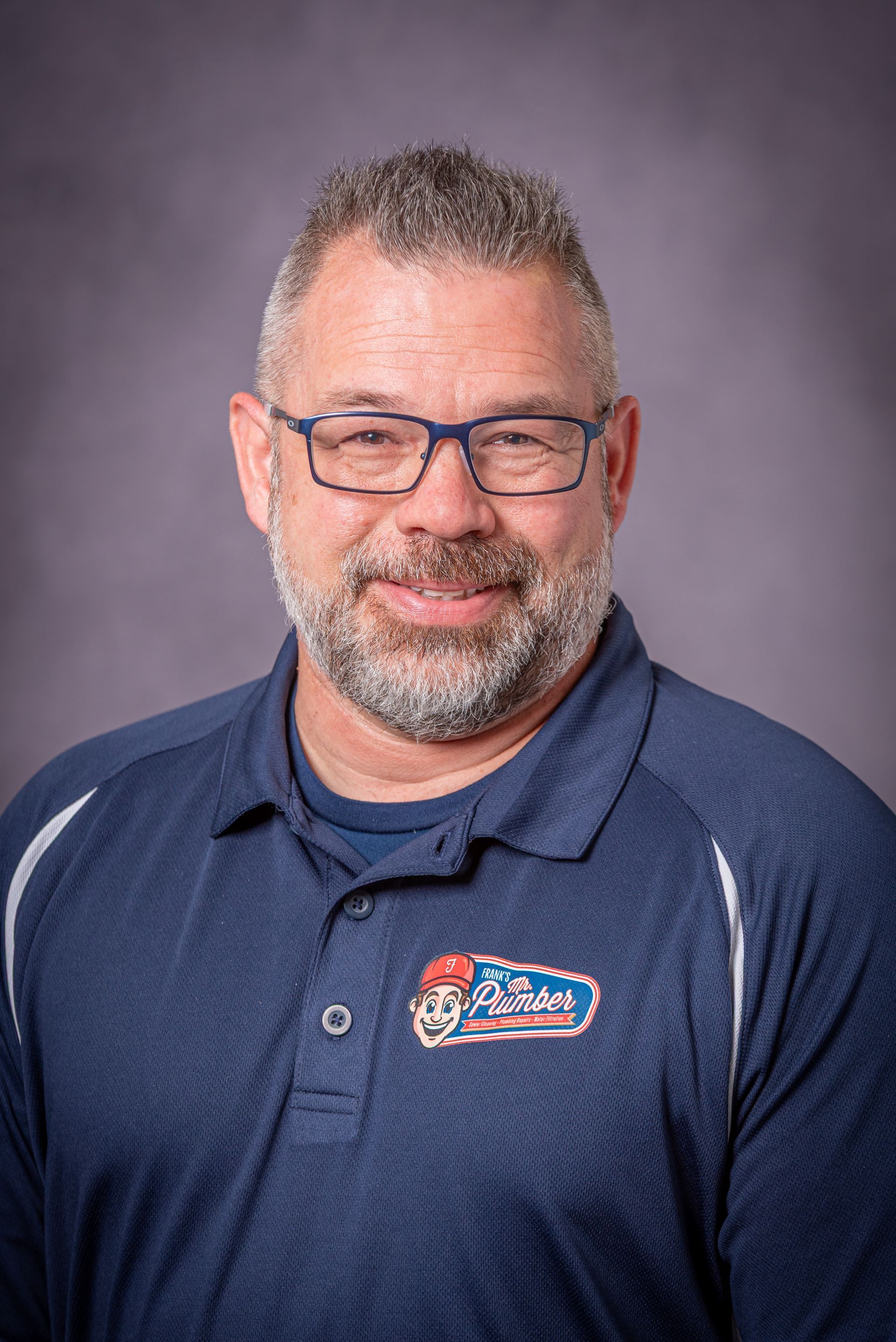 A man with a beard and glasses is wearing a blue polo shirt.