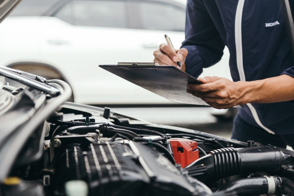 A Mechanic is Writing on a Clipboard While Looking Under the Hood of a Car — Auto Blue Service Centre In Bungalow, QLD