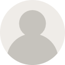 A person in a yellow raincoat and hat stands in a shallow stream, surrounded by colorful autumn leaves.