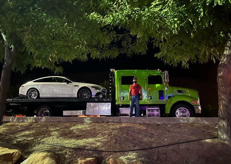 Black car being towed by a tow truck on an asphalt surface. The car's front tire is on a ramp.
