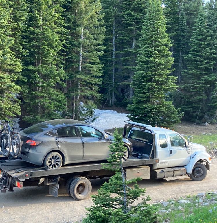 Two men loading a silver car onto a flatbed tow truck on a roadside.