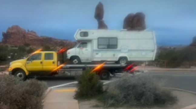 A damaged silver car loaded on a tow truck on a road.