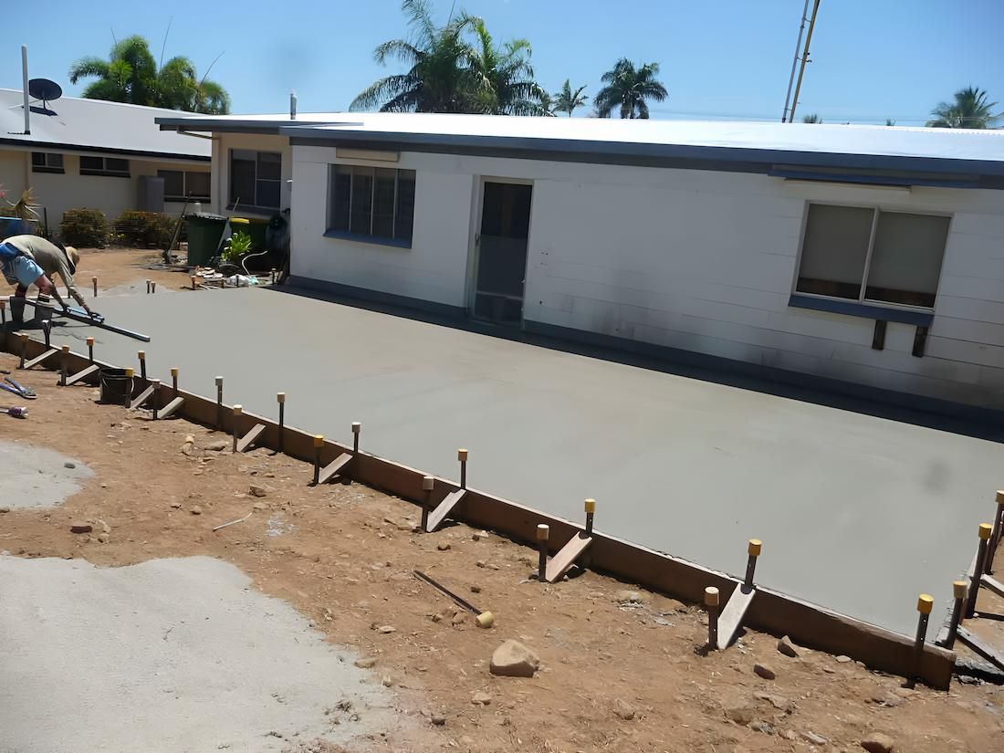 A Man Is Working On A Concrete Driveway In Front Of A House — Tropical North Concreting In Trinity Park, QLD