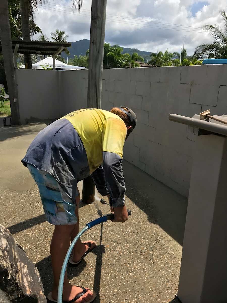 A Man Is Bending Over To Reach For A Hose — Tropical North Concreting In Trinity Park, QLD
