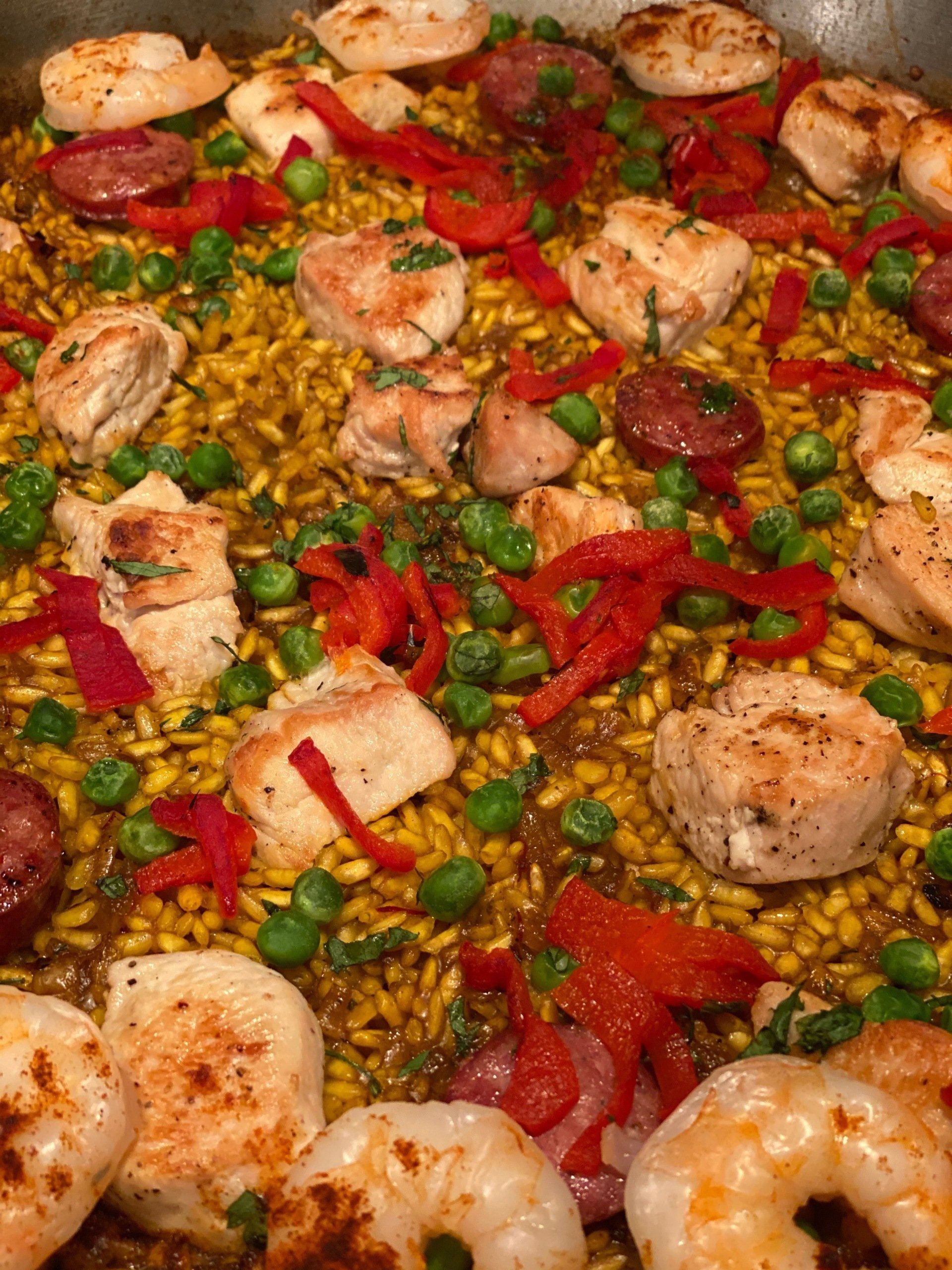 A close up of a paella with shrimp , chicken , peppers and peas.