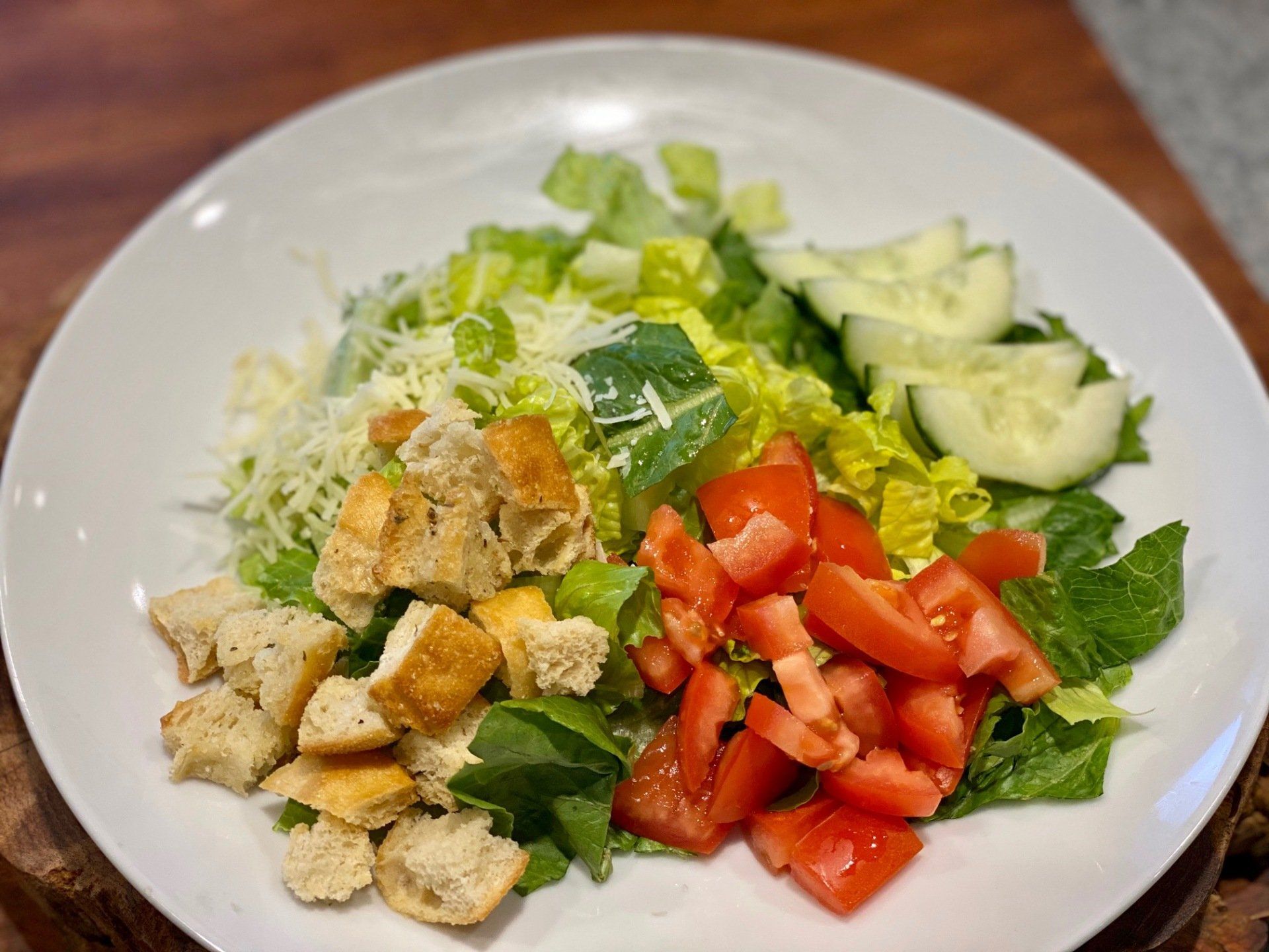 A white plate topped with a salad of lettuce , tomatoes , cucumbers and croutons.