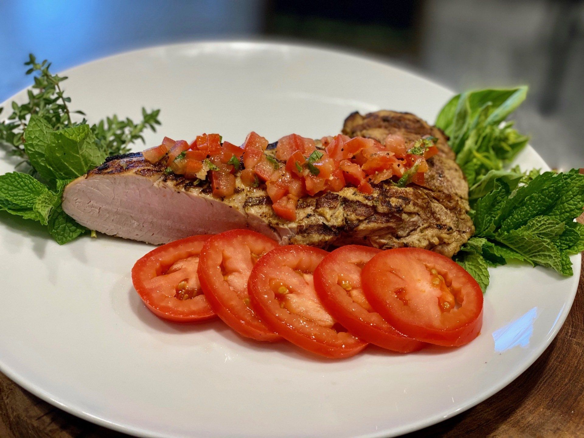 A white plate topped with meat and tomatoes on a wooden table.