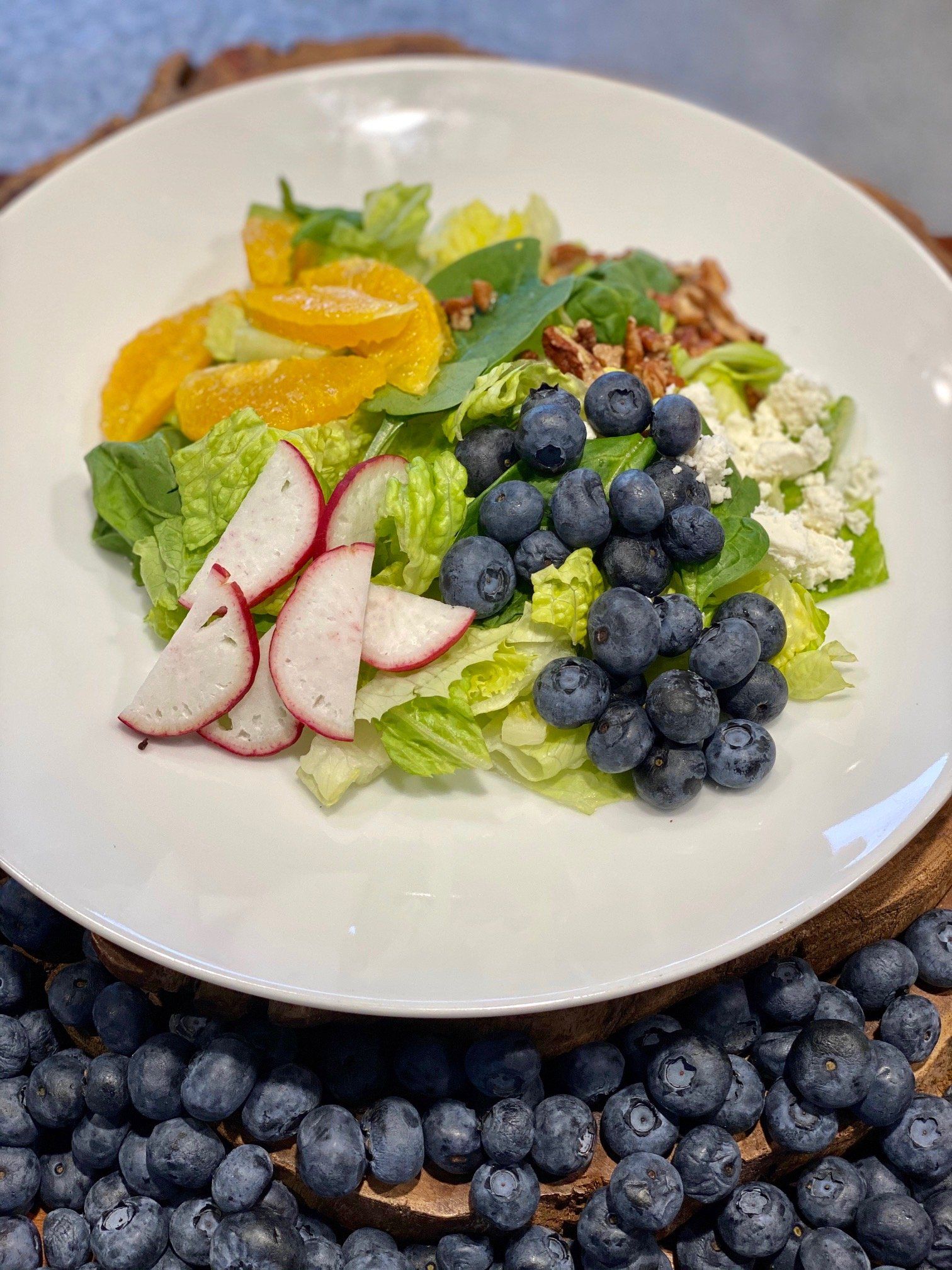 A white plate topped with a salad and blueberries on a table.
