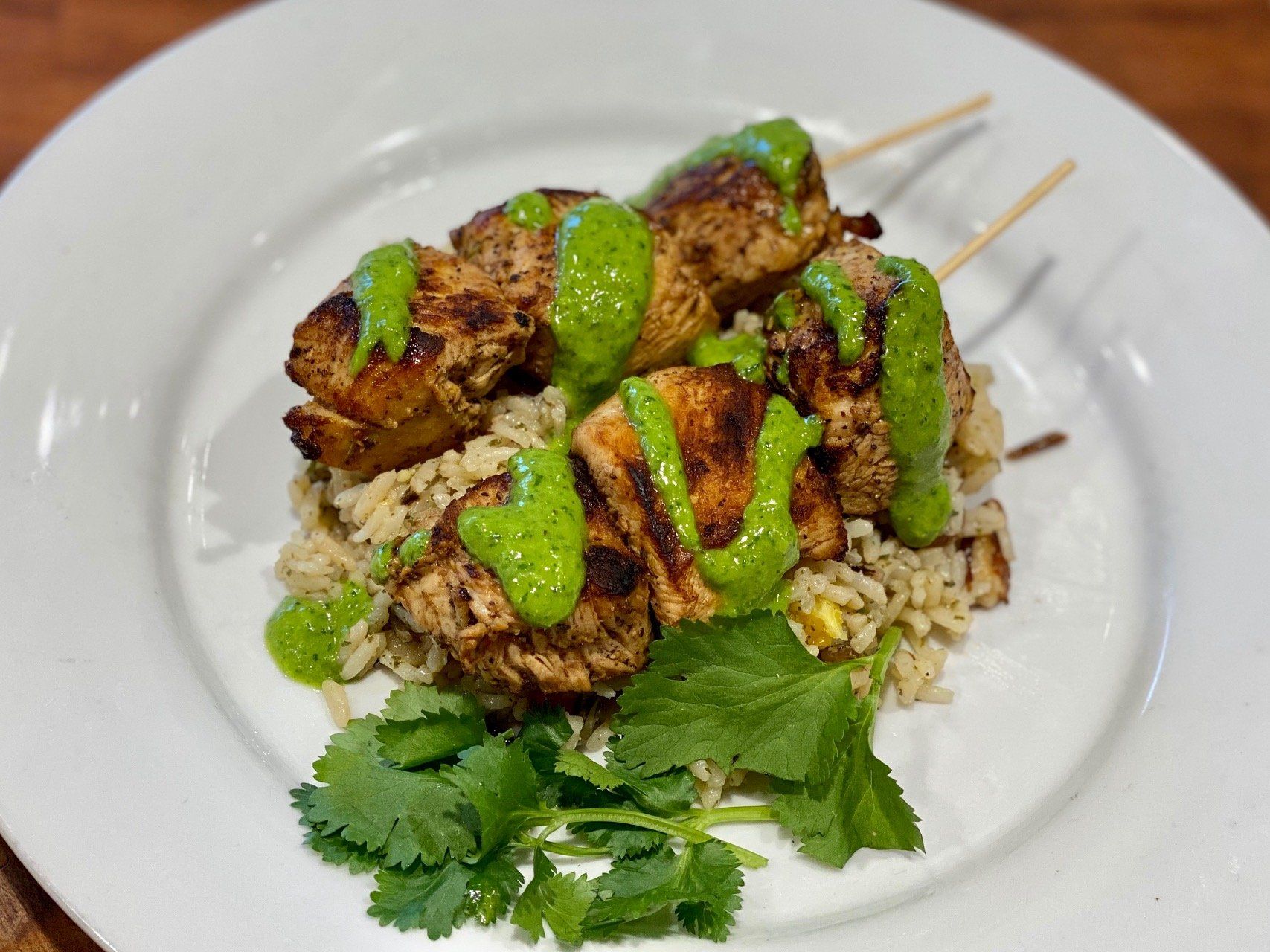 A white plate topped with chicken skewers and rice on a wooden table.