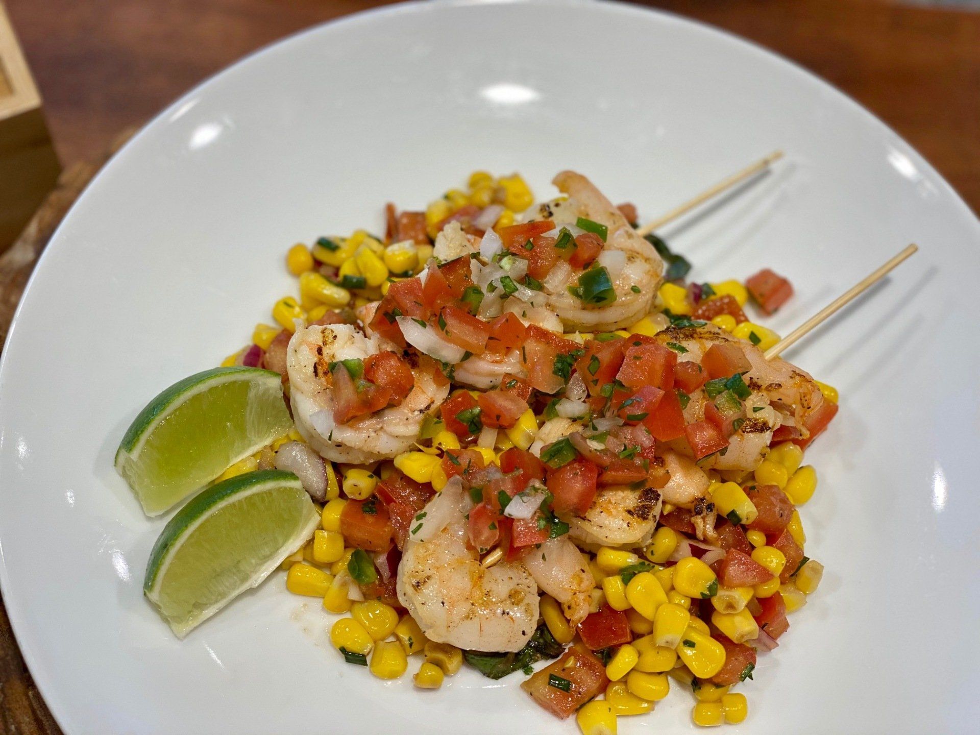 A white plate topped with shrimp , corn , tomatoes and lime wedges.