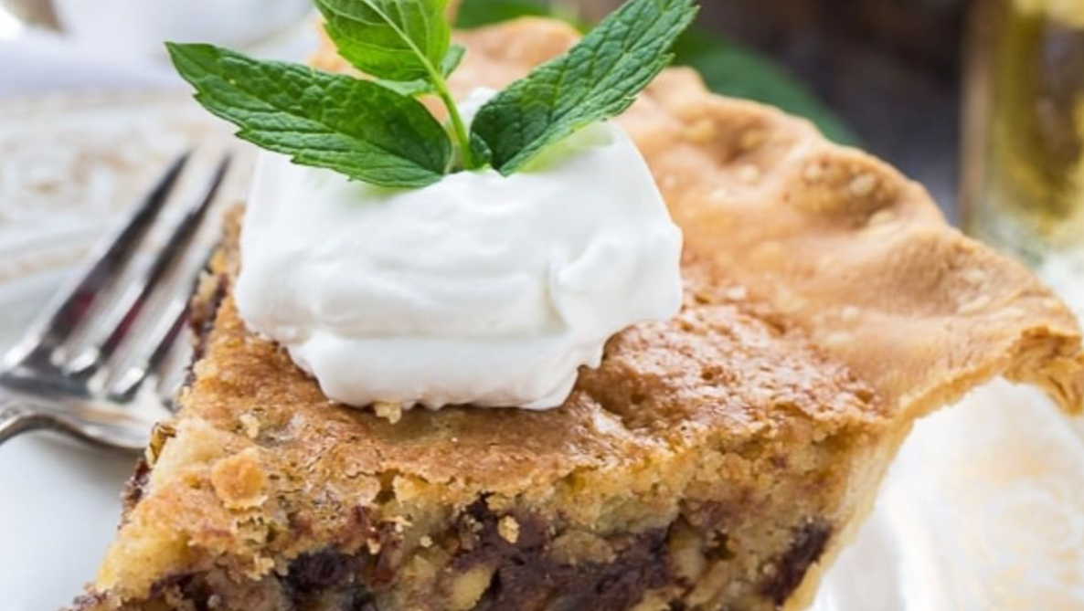 A slice of pie with whipped cream and mint leaves on top on a plate with a fork.