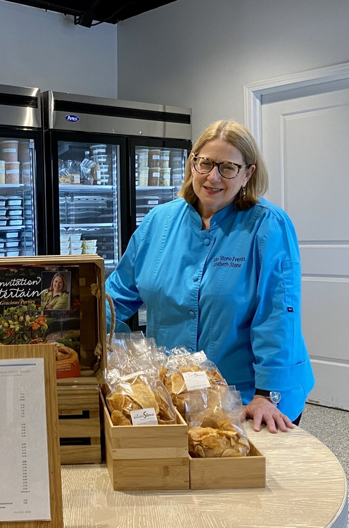 A woman in a blue jacket is standing behind a table with boxes of food.