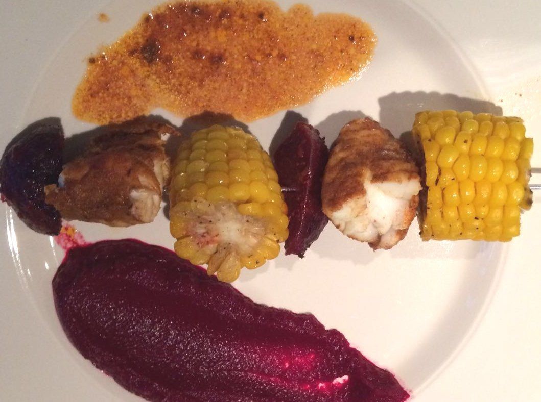 Grilled corn, fish, and beets on a white plate with reddish-brown and dark red sauces.