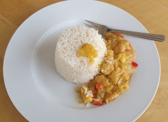 White plate with a mound of white rice, yellow sauce with shrimp, and a fork.