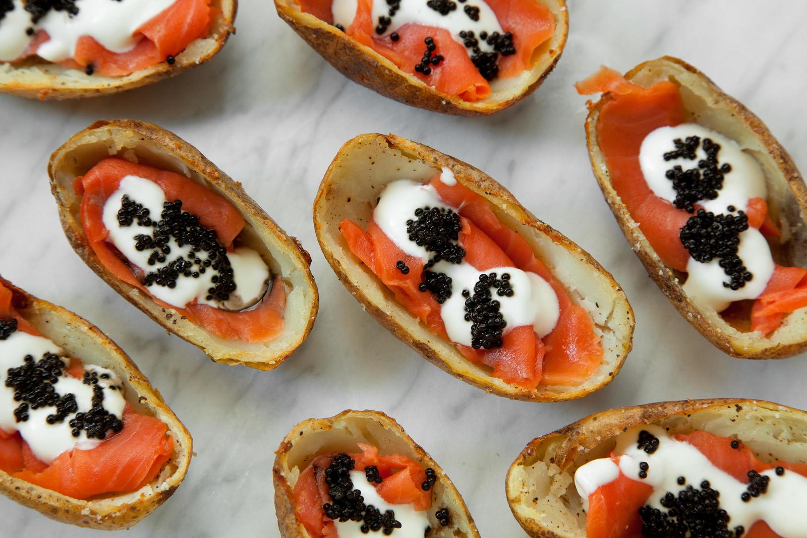 Potato skins with salmon, sour cream, and black caviar, arranged on a marble surface.