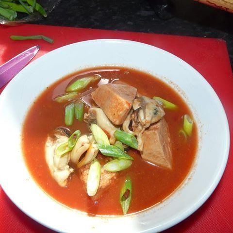 Bowl of red soup with tofu, mussels, and green onions.