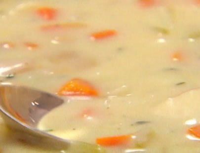 Creamy soup with visible carrots and potatoes being scooped with a spoon.