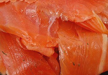 Close-up of thin, orange-red smoked salmon slices, with visible texture and some herbs.