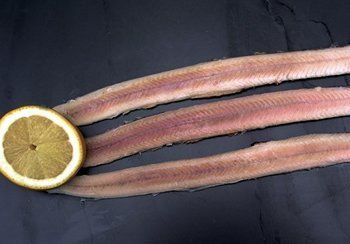 Three pale fish fillets and a lemon slice on a dark surface.