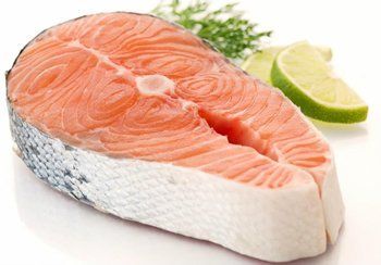 Salmon steak, cut with visible flesh and skin; lime and herbs in background.