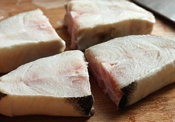 Four white fish steaks on a wooden cutting board, with visible grain and red marbling.