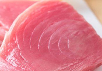Close-up of fresh, pink raw tuna steak, showing textured grain and glistening surface.