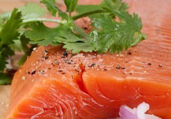 Close-up of raw salmon fillet, sprinkled with salt and pepper, garnished with cilantro.