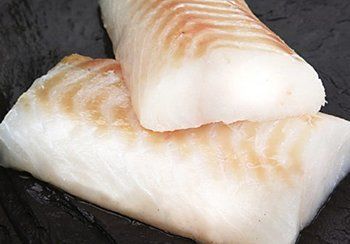 Two raw cod fillets, white with tan striations, on a dark surface.
