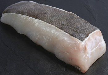 Halibut fillet with dark skin on one side, pale flesh on the other, on a dark surface.