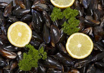 Mussels in dark shells, garnished with lemon slices and parsley.