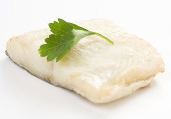 Cooked white fish fillet with a sprig of green parsley.