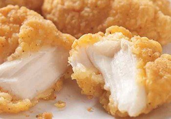 Close-up of a chicken nugget, golden-fried exterior, revealing white, cooked chicken inside.
