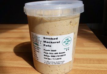 Smoked mackerel pate in a clear plastic tub on a wooden surface. The label lists the product and a 