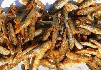 Pile of fried small fish, golden brown, on a white surface.