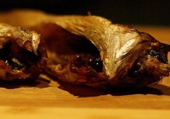 Smoked fish cut open, showing dark eyes and flesh against a wooden surface.